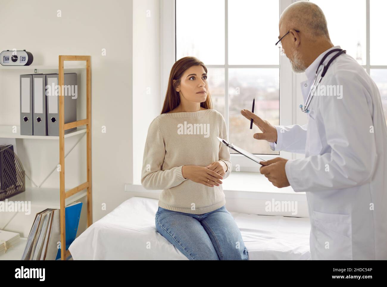 Senior doctor trying to calm down worried young woman before medical exam at clinic Stock Photo