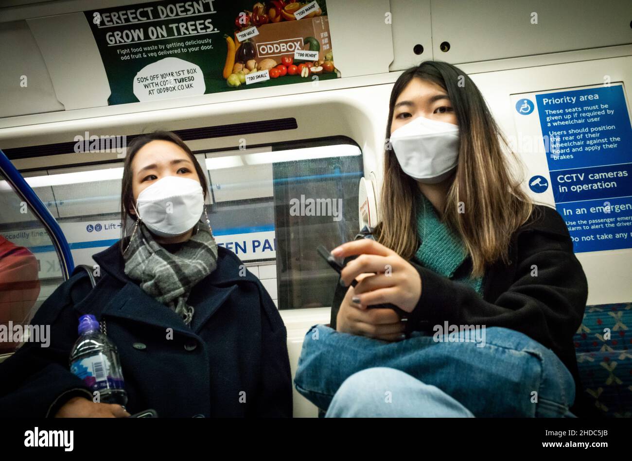 Two young Chinese women wearing face masks sit on a tube train at Green Park underground station in London, UK Stock Photo