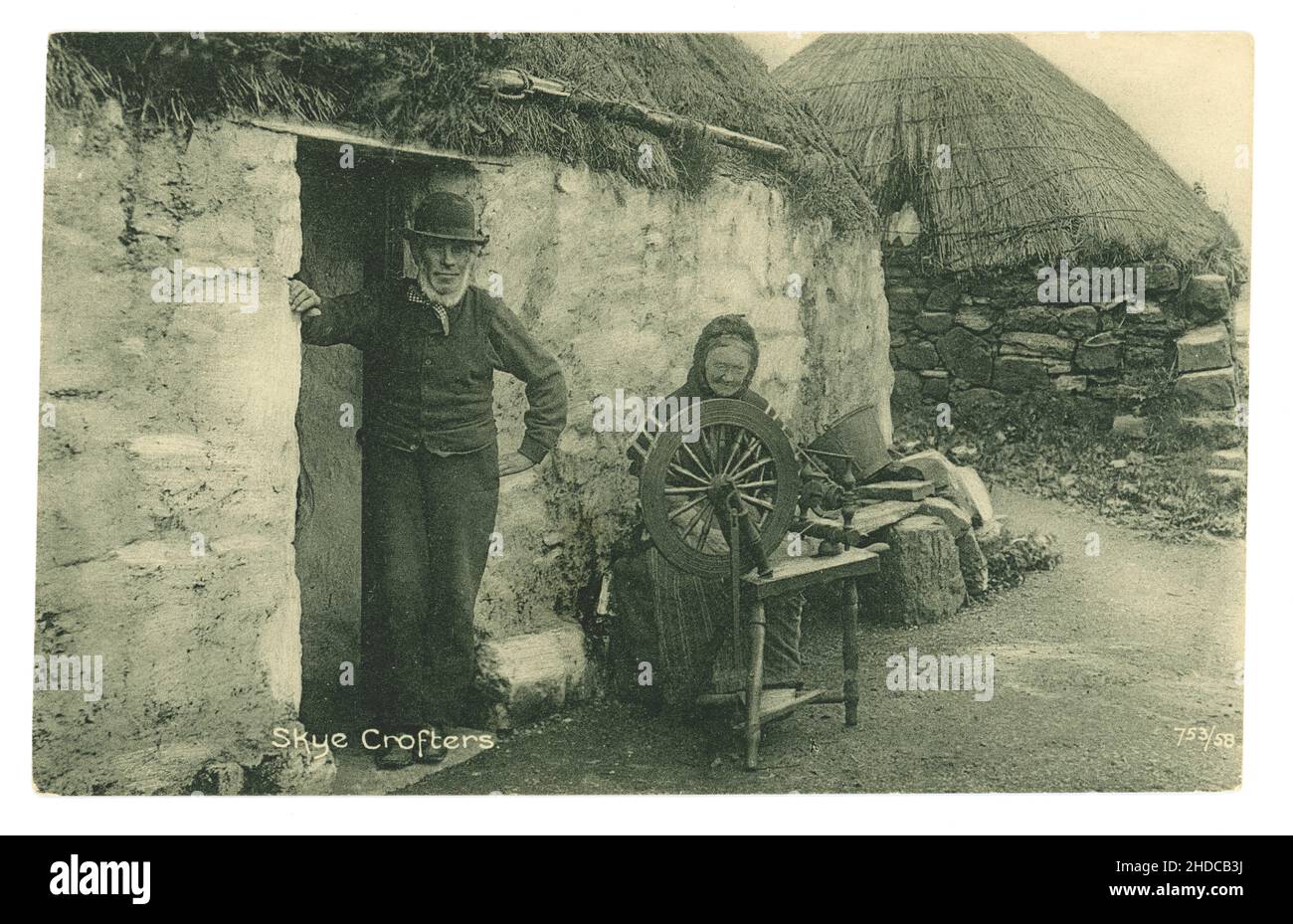 Original early 1900's Edwardian era postcard of Skye crofters, tenant farmers, outside their croft, the old woman has a spinning wheel and is spinning wool - subsistence living. Printed by the Reliable series by W R & S William Ritchie and sons - circa 1905. Isle of Skye, Inner Hebrides, Scotland, U.K. Stock Photo