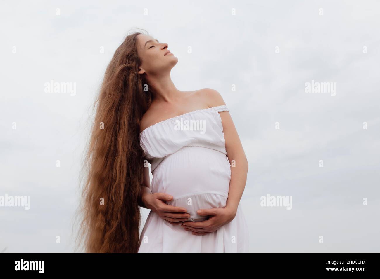 Happy pregnant woman in white dress on a green meadow Stock Photo