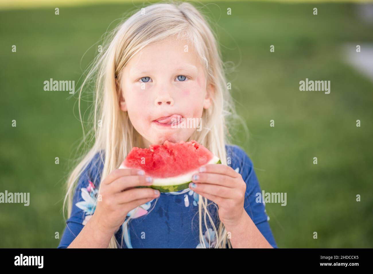 Young girl licking her lips while eating watermelon slice outside Stock Photo