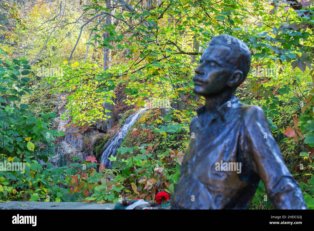 Miskolc, Hungary – October 26, 2019: Waterfall in beautiful autumn castle park of Lillafured. Blurred monument to famous Hungarian poet Jozsef Attila Stock Photo