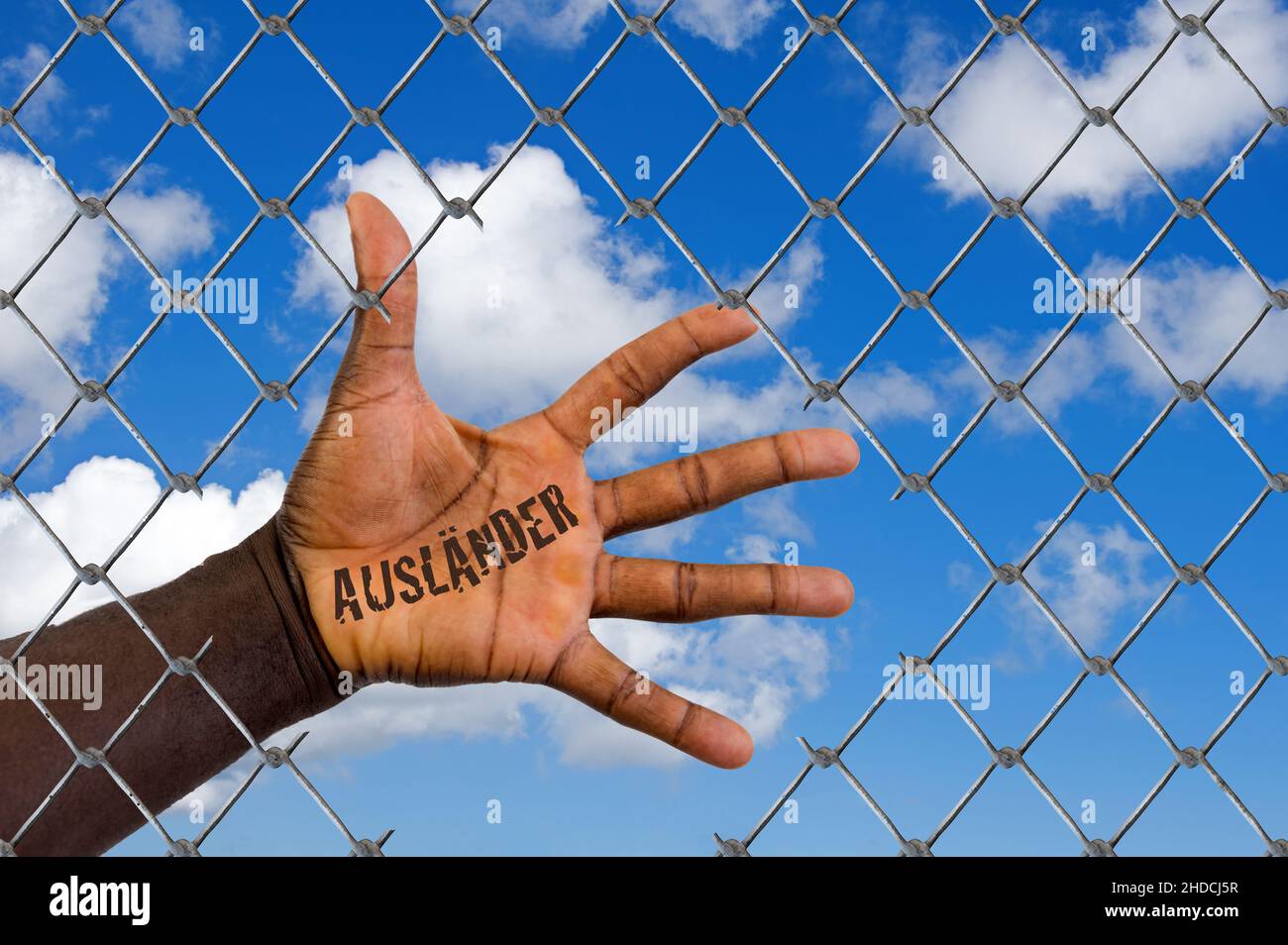 Die Hand eines Migranten hinter einem Maschendrahtzaun, Loch, Schlupfloch, Hilfe, Flüchtling, Asyl, Migrant, Migration, Ausländer, Schwarz, Afrikaner, Stock Photo