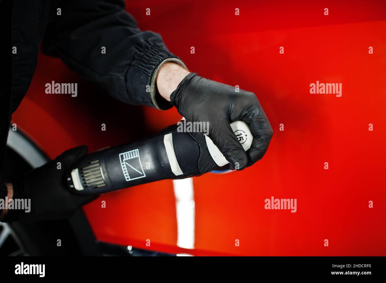 Car detailing concept. Hands of man with orbital polisher in repair shop polishing orange suv car. Stock Photo