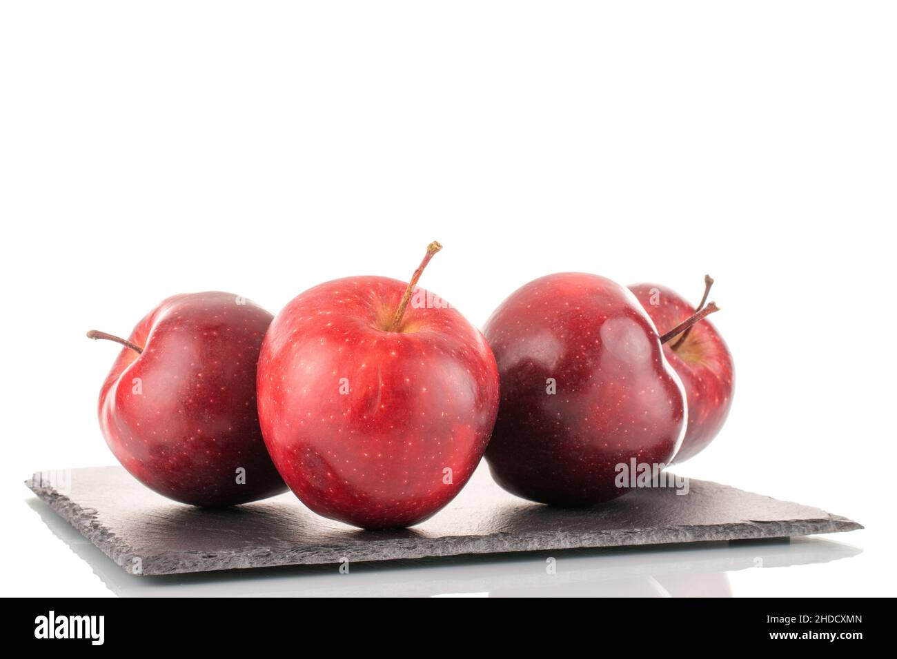 Four ripe sweet, red apples on a slate stone, close-up, isolated on white. Stock Photo