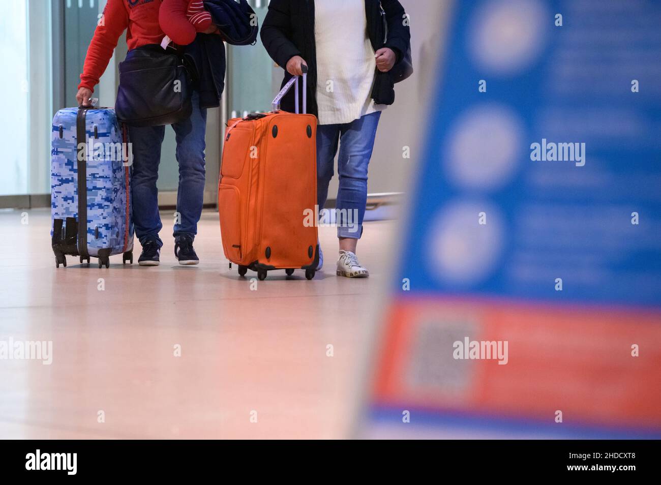 Hamburg, Germany. 04th Jan, 2022. Returning passengers of the cruise ship 'Aidanova' walk with their suitcases through the arrivals area of Hamburg airport in the night in front of a sign with notices about the Corona measures after they had been flown back to Germany in one of two charter flights. Aida Cruises had decided to cancel the voyage of the 'Aidanova' in Lisbon after the cases of infection and not to continue as planned until Wednesday towards the Canary Islands. Credit: Jonas Walzberg/dpa/Alamy Live News Stock Photo