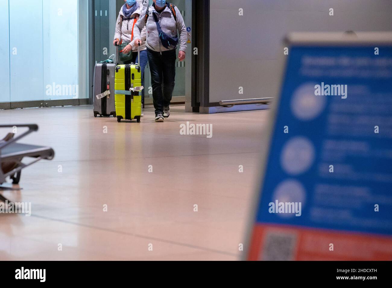Hamburg, Germany. 04th Jan, 2022. Returning passengers of the cruise ship 'Aidanova' walk with their suitcases through the arrivals area of Hamburg airport in the night in front of a sign with notices about the Corona measures after they had been flown back to Germany in one of two charter flights. Aida Cruises had decided to cancel the voyage of the 'Aidanova' in Lisbon after the cases of infection and not to continue as planned until Wednesday towards the Canary Islands. Credit: Jonas Walzberg/dpa/Alamy Live News Stock Photo