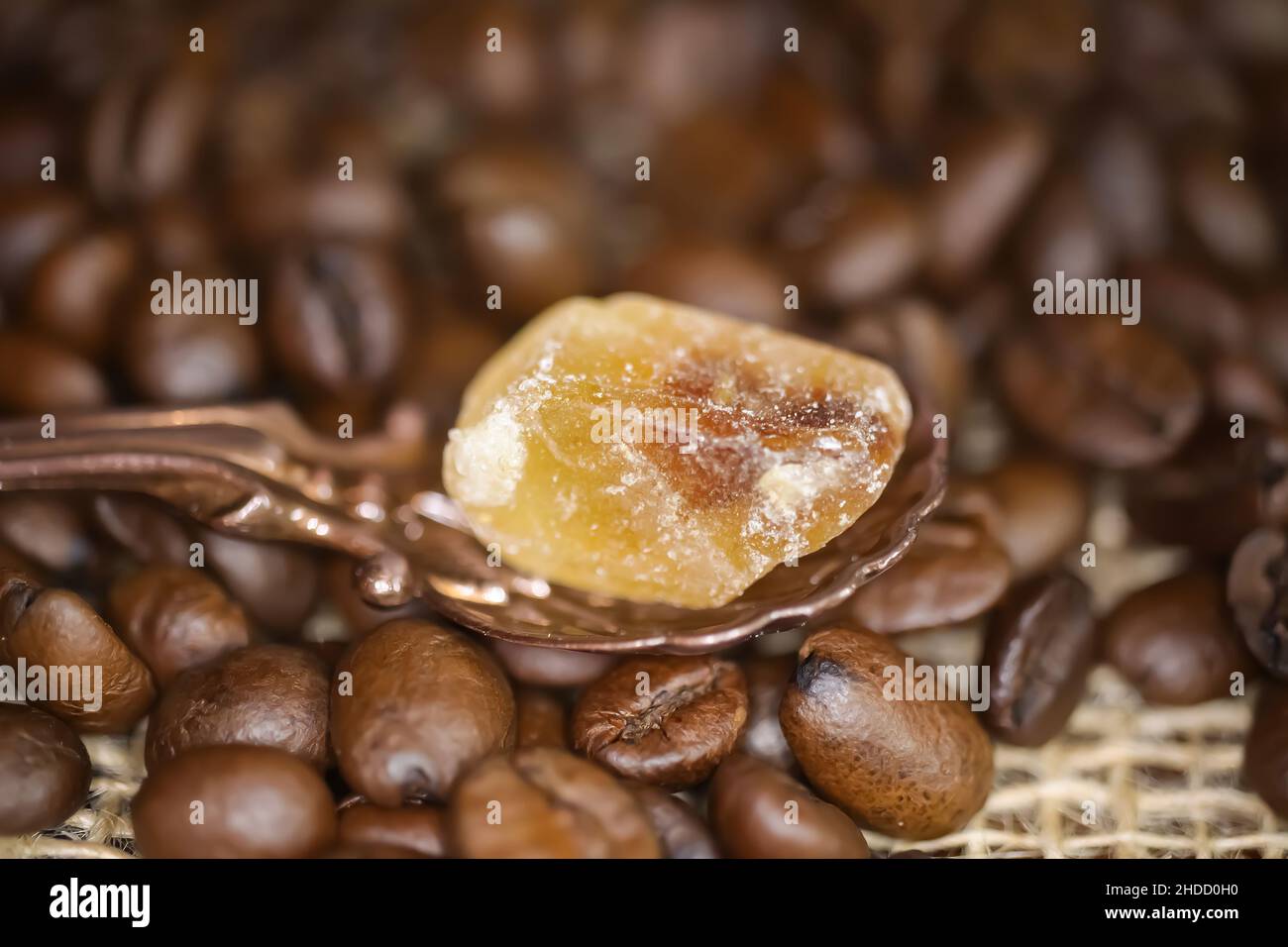 Closeup of vintage bronze spoon with one single cube brown rock candy sugar, blurred roasted coffee beans background Stock Photo