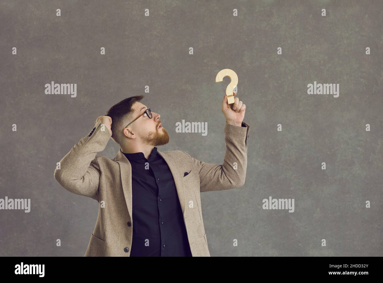 Confused businessman holding a question mark and thinking of an answer to a question Stock Photo