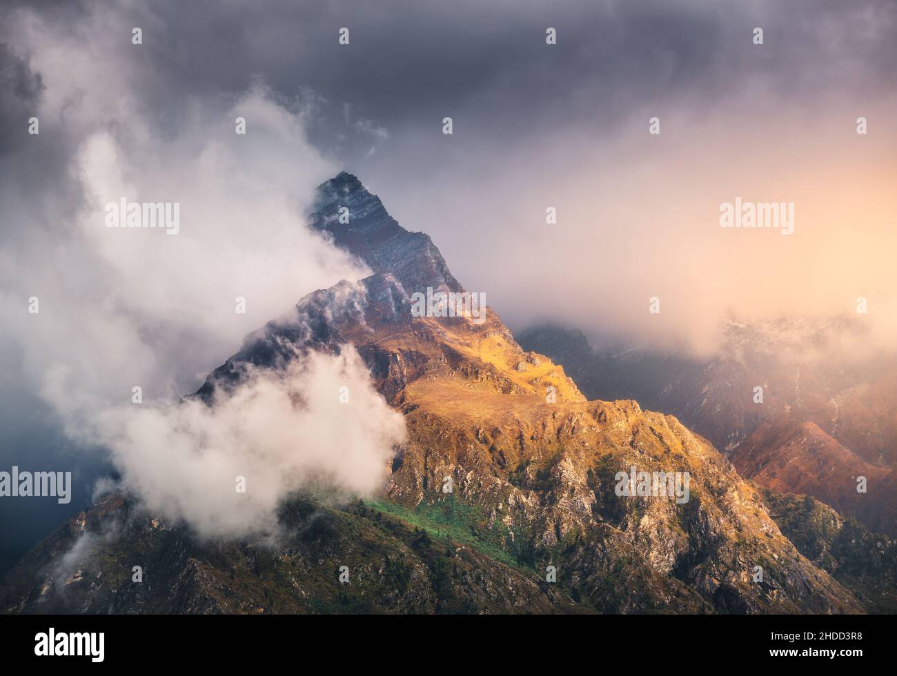 Mountain peak in low clouds at colorful sunset in Nepal Stock Photo
