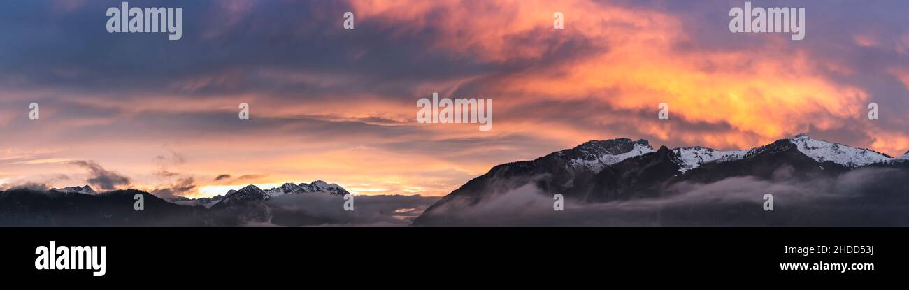 fog covered hahnenkamm mountain range with dramatic orange-red sky at sunset in late autumn Stock Photo