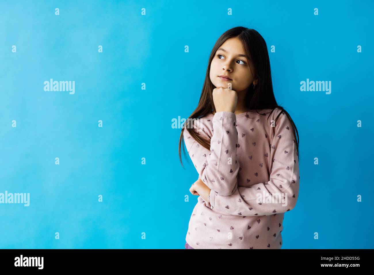 Portrait of girl thinking touching chin isolated over turquoise color background Stock Photo