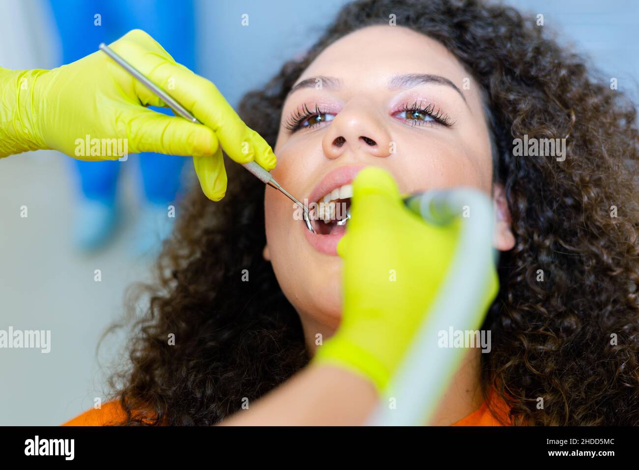 Beautiful mixed-race teenage girl  having tooth drill procedure at dental office. Hands in green protective gloves holding instruments. Stock Photo