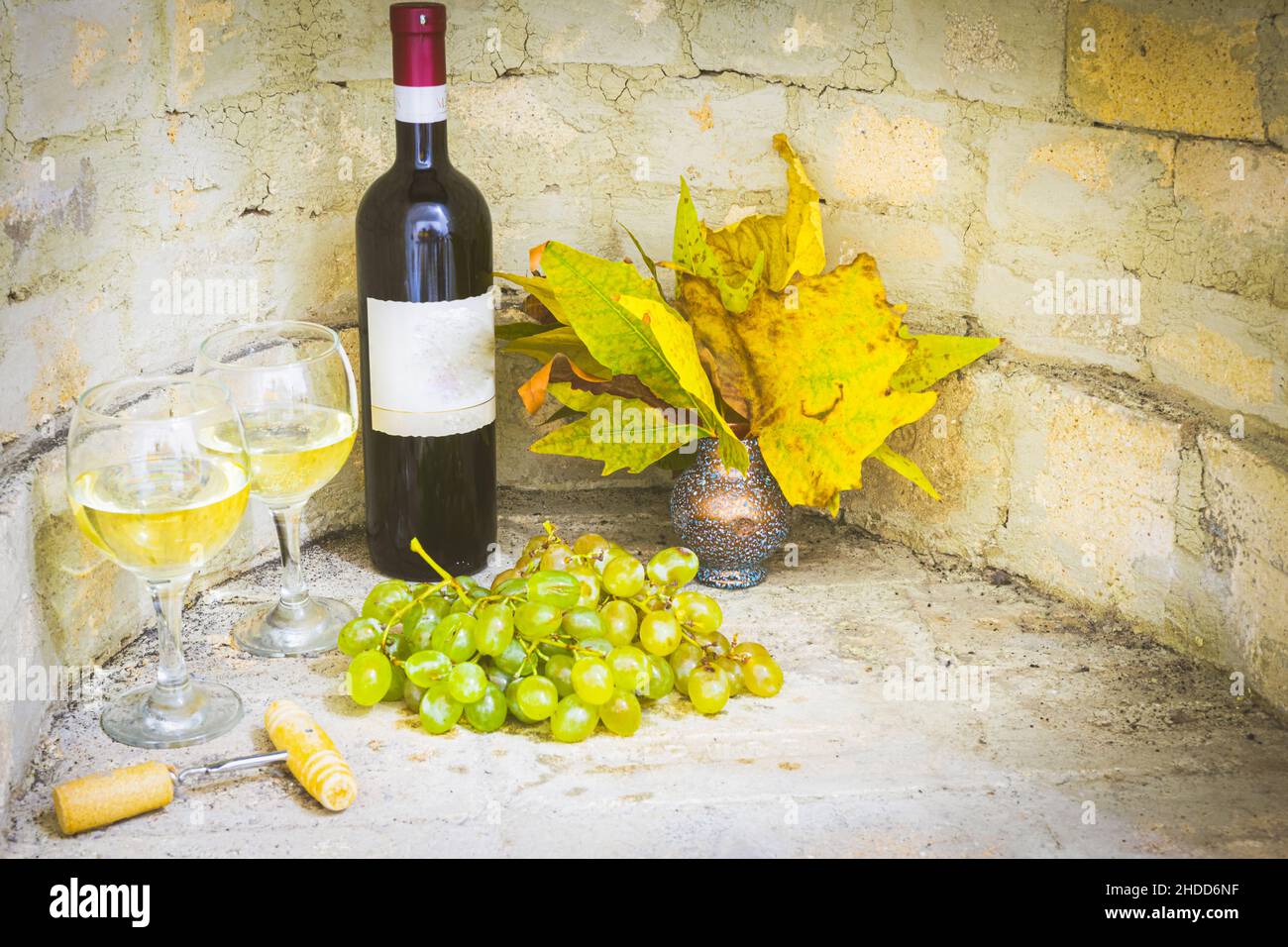 Set up of red bottle of wine with full glasses, green grapes and autun leafs in vase with blank space bacground of brick wall. Stock Photo