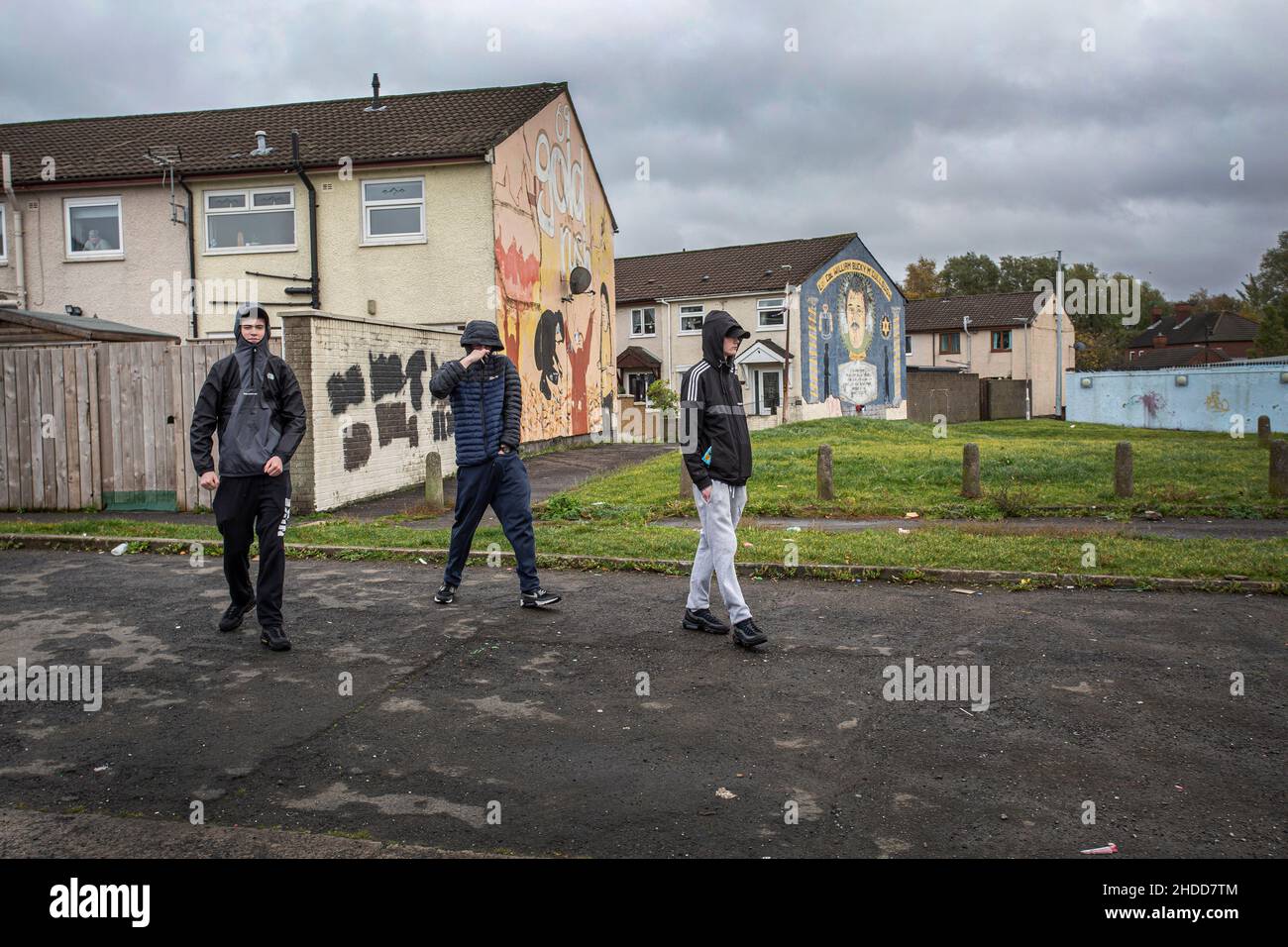Youths walking in front of political murals with paramilitary symbols on the Lower Shankill Estate, Belfast. Stock Photo