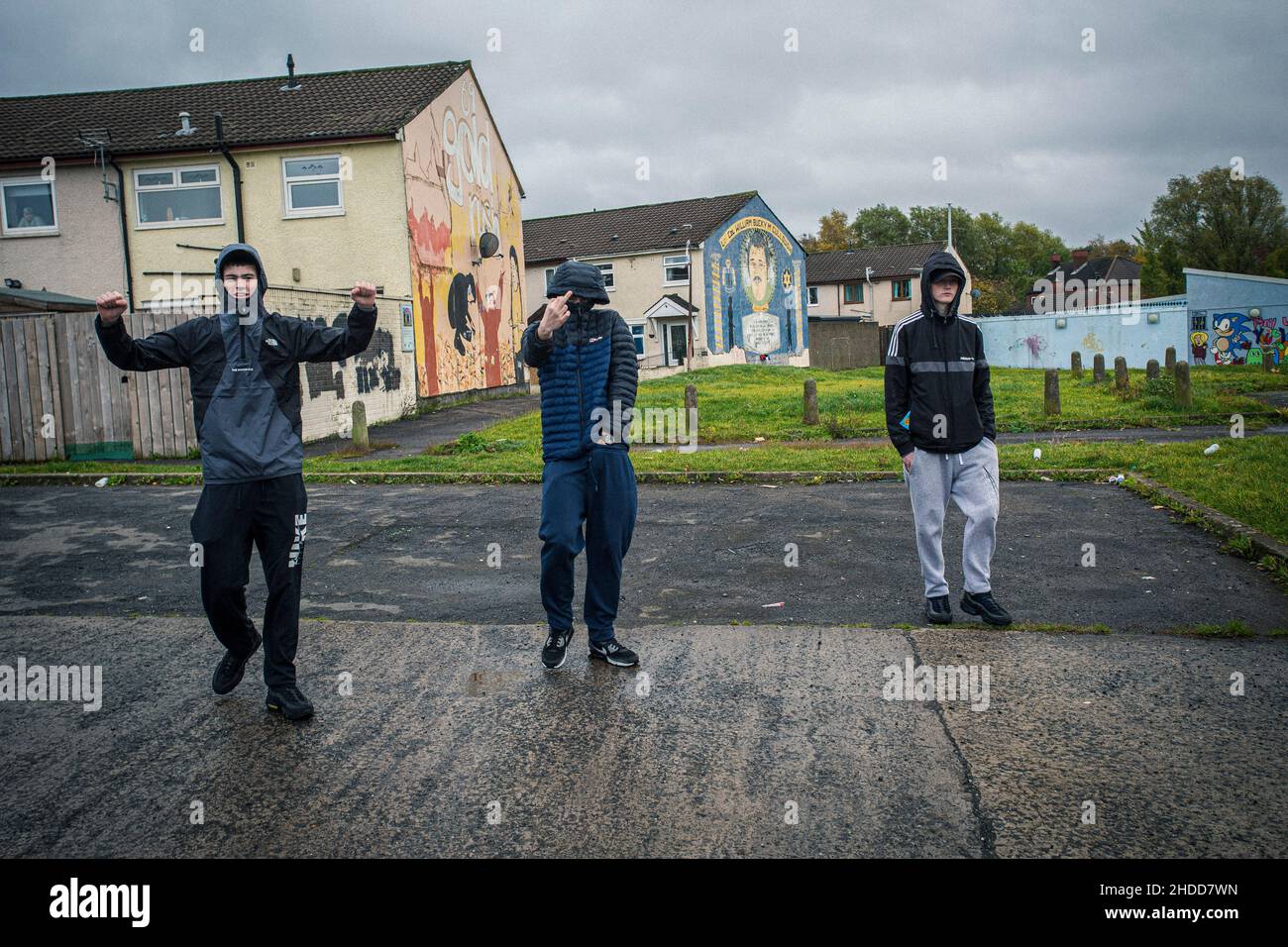 Youths walking in front of political murals with paramilitary symbols on the Lower Shankill Estate, Belfast. Stock Photo