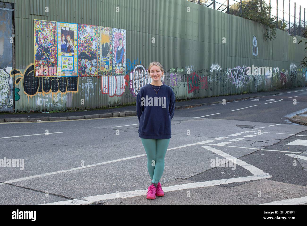 Amy Rafferty from Trademark, Community Organisation outside her office with colourful murals & graffiti on Peace wall,or Peace Line, running along Cup Stock Photo