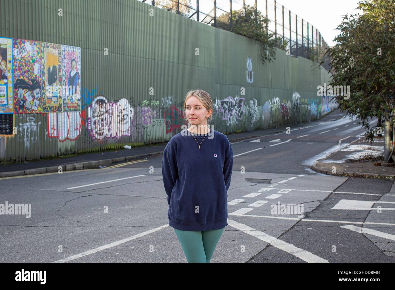 Amy Rafferty from Trademark, Community Organisation outside her office with colourful murals & graffiti on Peace wall,or Peace Line, running along Cup Stock Photo