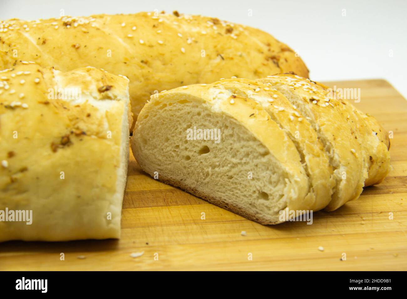 Wheat bread baked from flour at home. Sliced bread on wooden board  against background. Food with NO GMO. Homemade bread with spice on it. Stock Photo