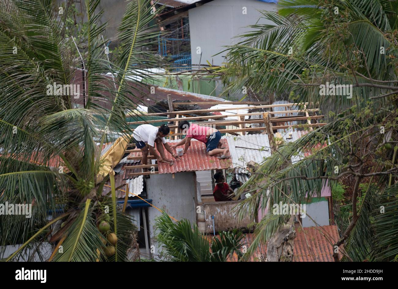 Two men fixing the roof of a house severely damaged by Typhoon Odette (International name Rai) which struck the Philippines on 16th December 2021 Stock Photo