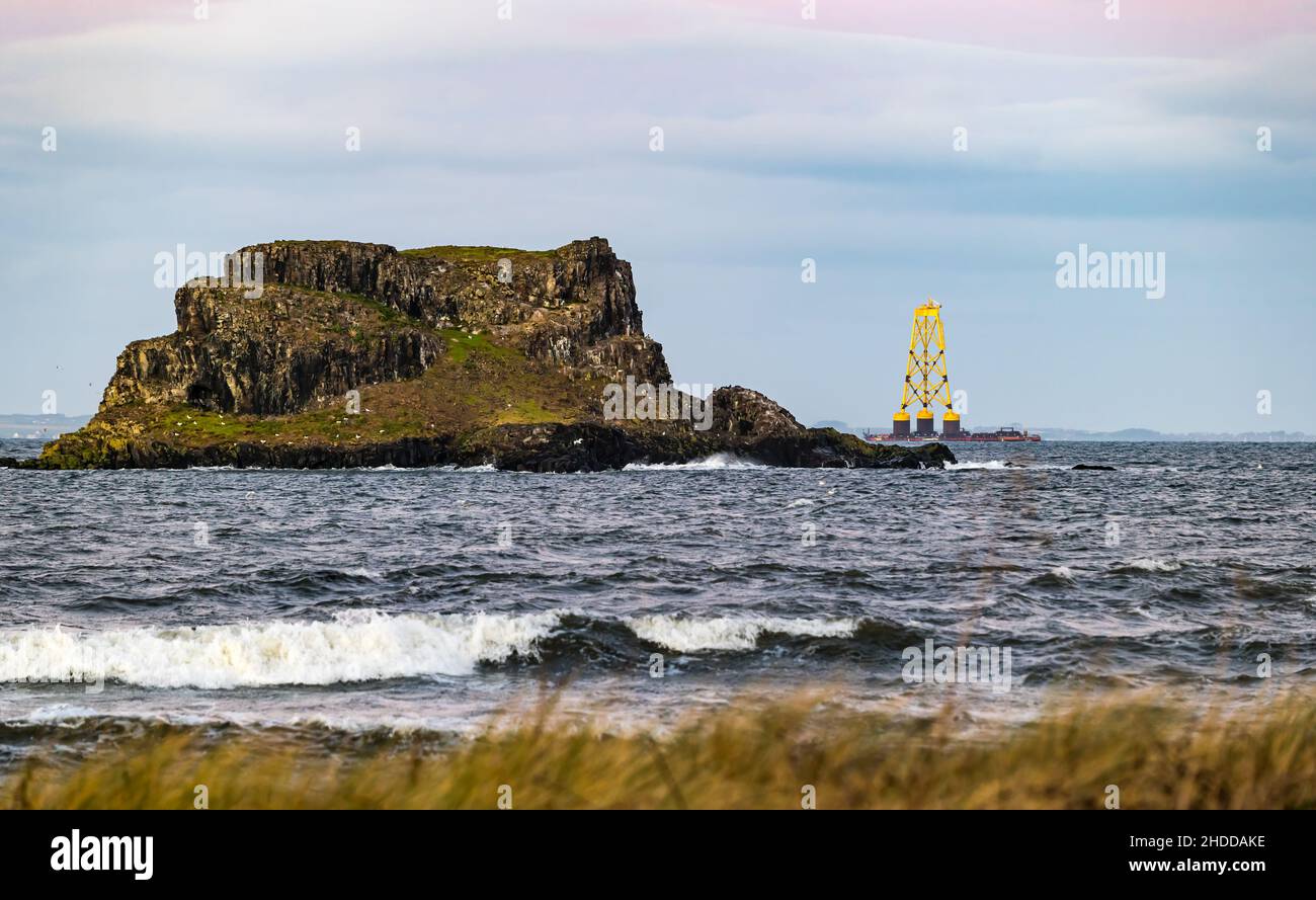 Firth of Forth, Scotland, 5th January 2022. UK Weather: a barge carrying an enormous wind turbine platform heads out to the North Sea at sunset past Fidra island Stock Photo