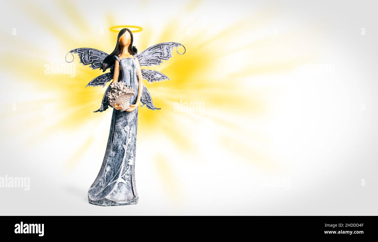 Angel with halo on yellow and white background. Statue of angel. Spiritual, faith, heaven. Guardian Angel on background with light rays of the sky. Stock Photo