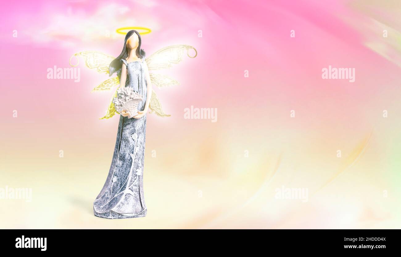 Angel with halo on colorful background (purle, yellow, gold) - heaven, clouds. Statue of angel with light rays of the wings. Spiritual, faith. Stock Photo