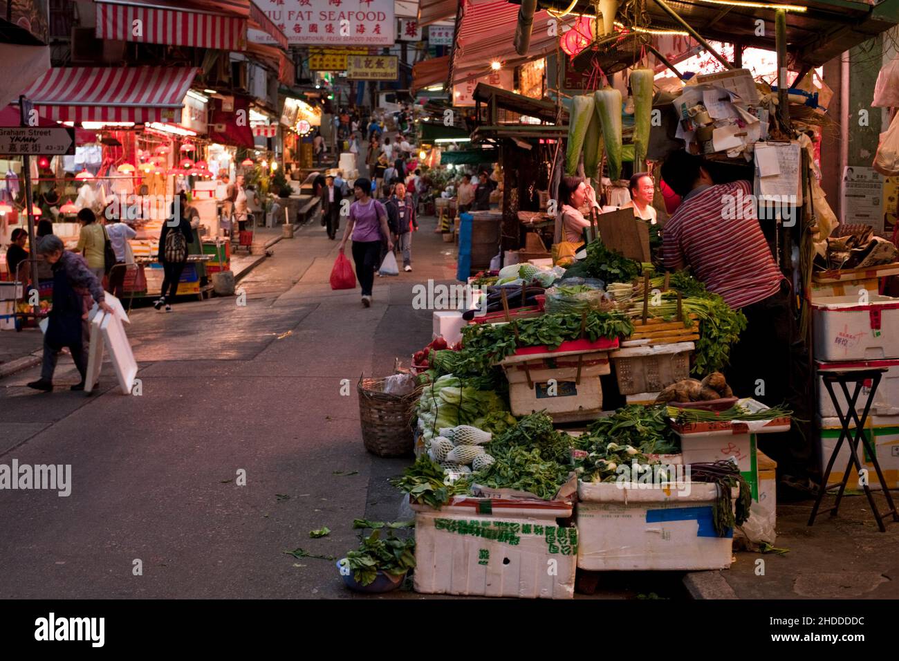 A market street in Hong Kong, with a vegetable stall in the foreground, as evening sets in. Stock Photo