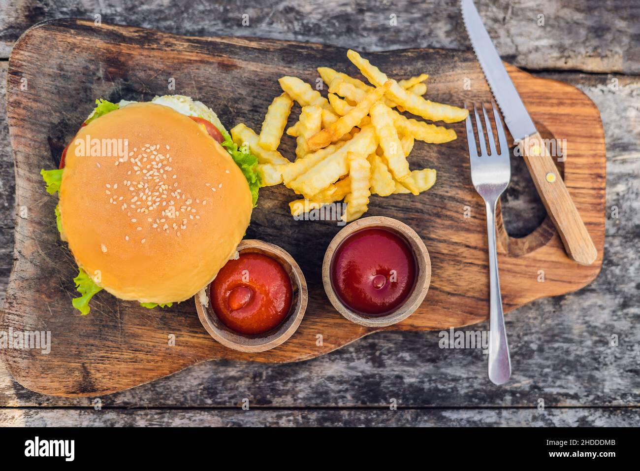 Closeup of fresh burger with French fries on wooden table with bowls of tomato sauce. lifestyle food Stock Photo