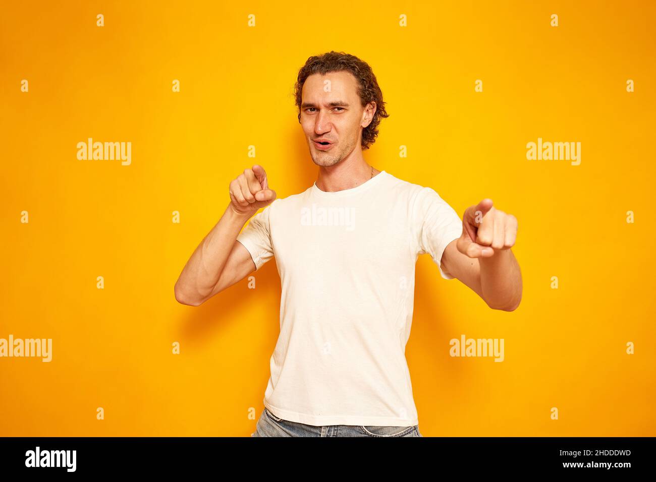 young, joyful, curly-haired man points his index fingers in front of him, hinting that you are best, winner. isolated yellow background with space for text. concept people, victory, advantage, delight. High quality photo Stock Photo
