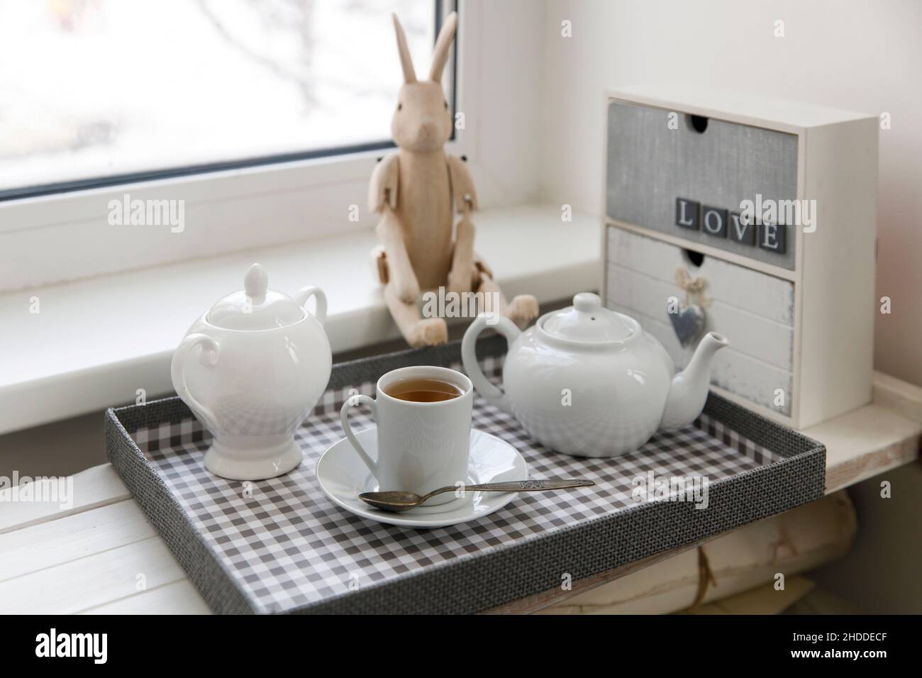 Tea drinking. A cup of tea, a sugar bowl and a kettle are on the tray. A small wooden chest of drawers with two drawers and the inscription 'Love', th Stock Photo