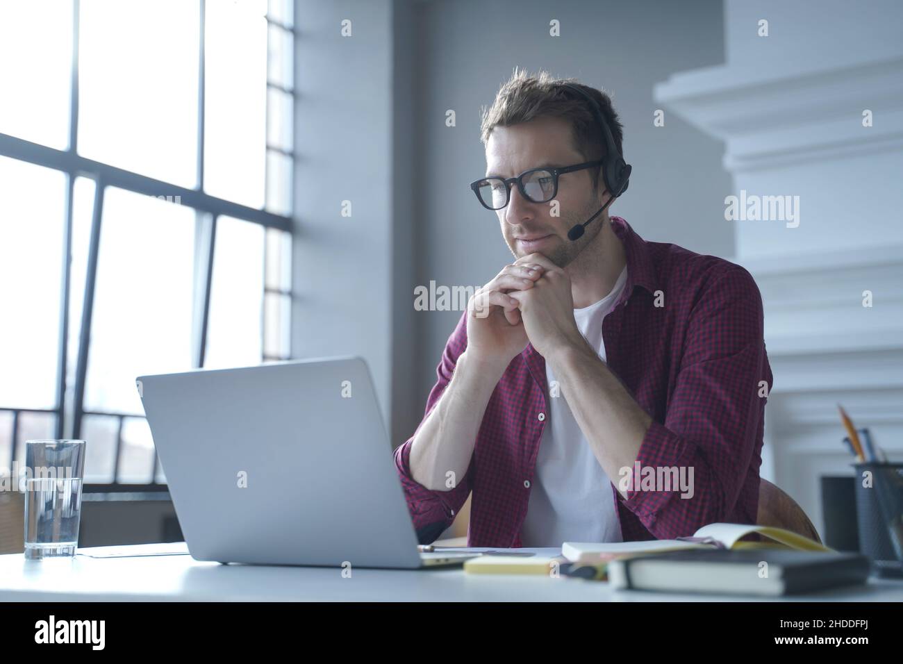 Pensive German businessman in headphones sits at desk while remotely working from home Stock Photo