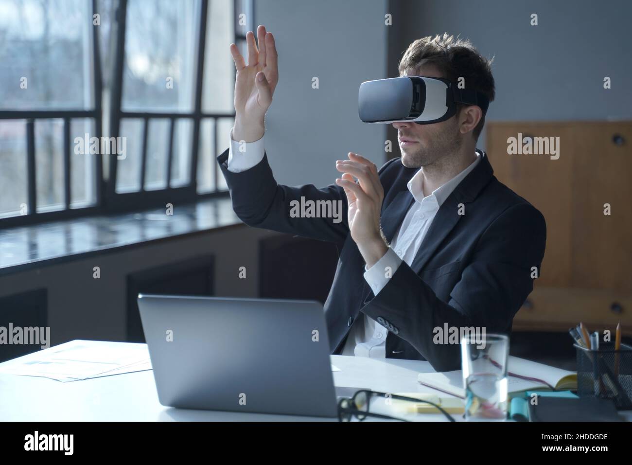 Male office worker in vr headset interacting with digital interface while sitting at desk Stock Photo