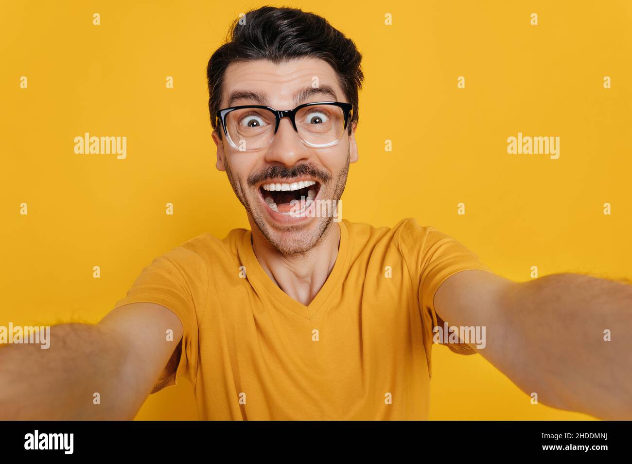 Funny caucasian guy in glasses, dressed in an orange Tshirt, makes a