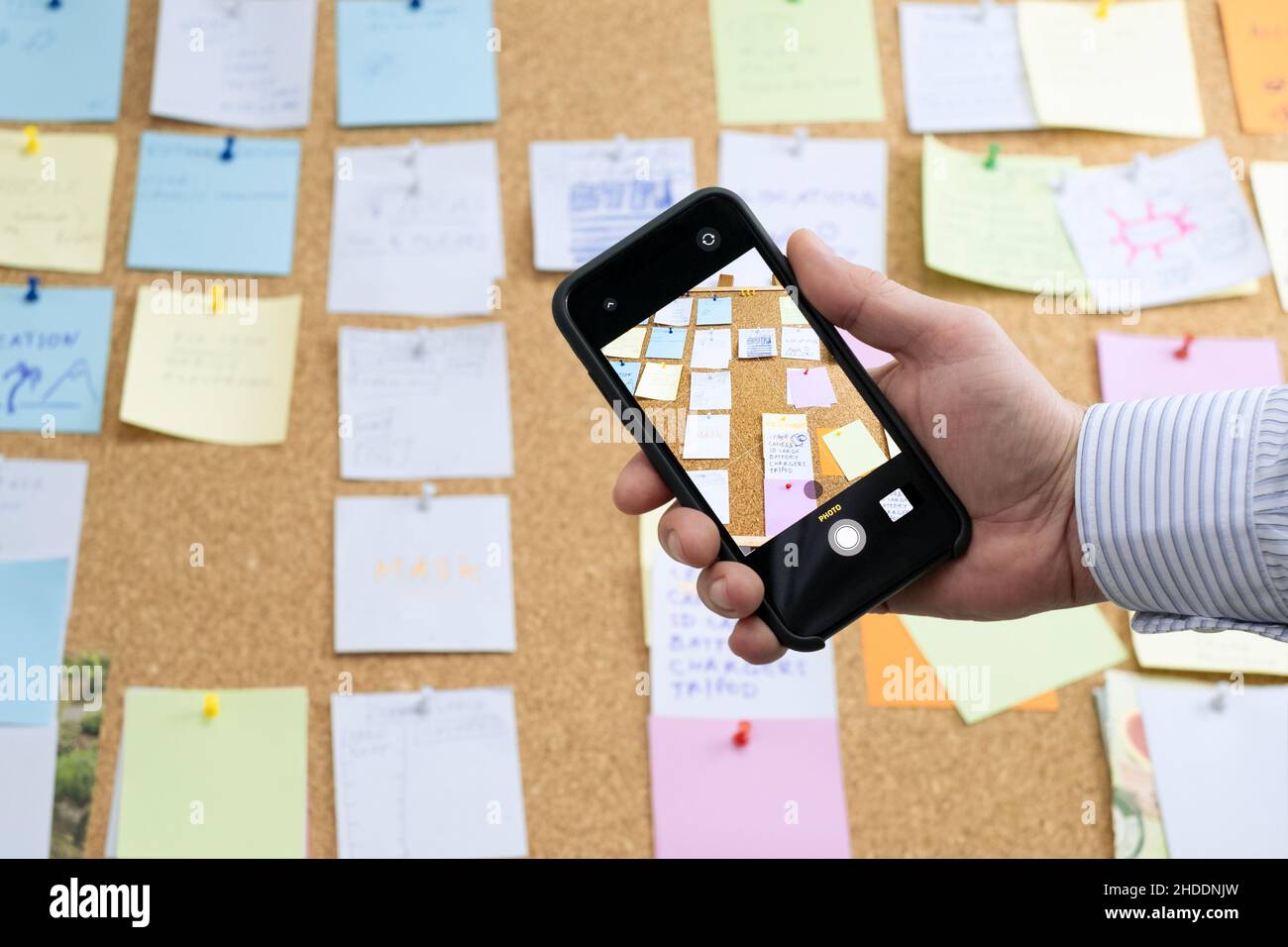 Photographing Using a mobile Smartphone for planning tasks and calendar events in the office, Sticky notes on a cork board in the background.  use of Stock Photo
