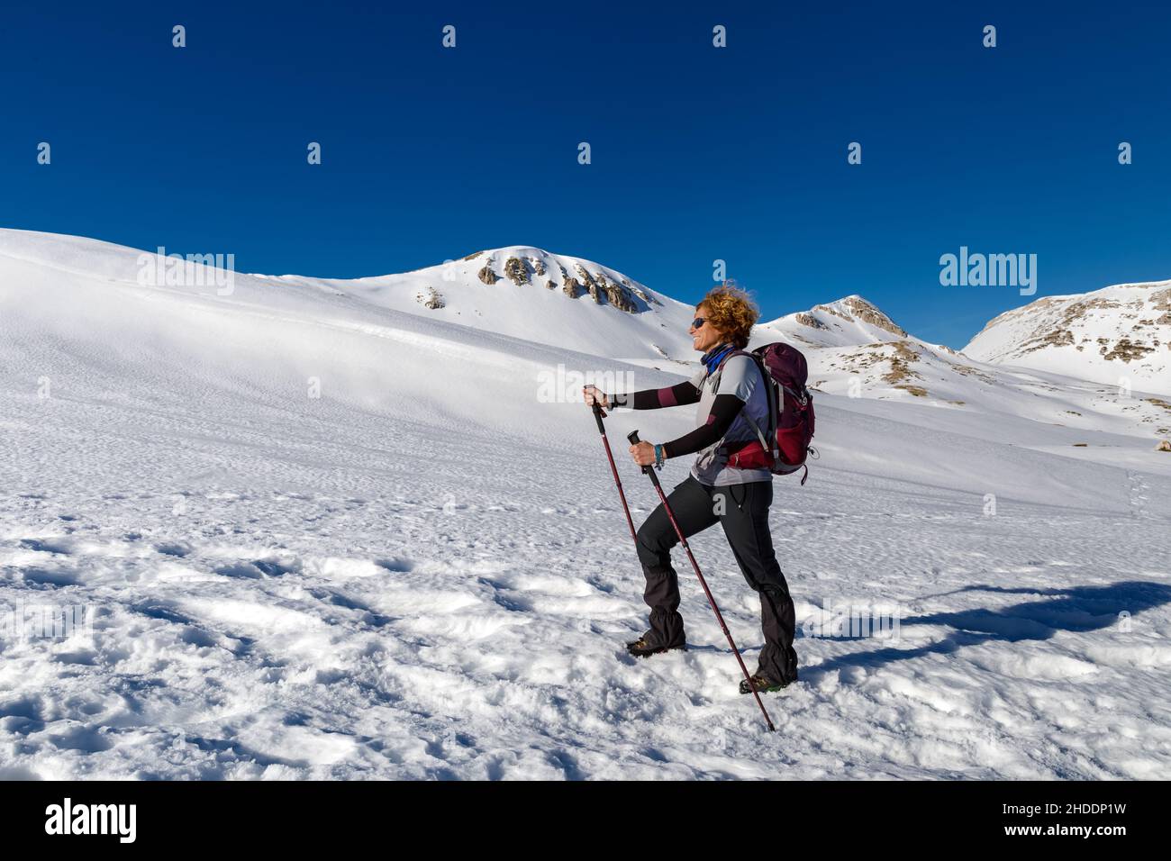 A woman walks alone on the snow in the mountains, towards the summit ...