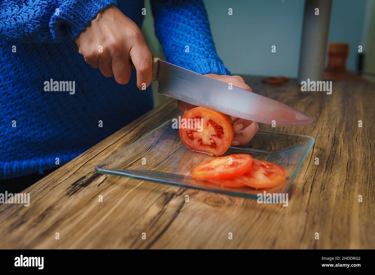 On the table there is a cutting board and you can see a woman's hands cutting white onions with a chef's knife. Stock Photo