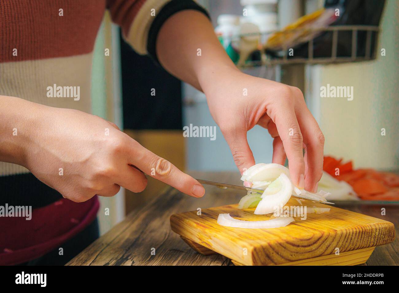 On the table you can see some hands cutting with a chef's knife a white onion, slices of onion Stock Photo