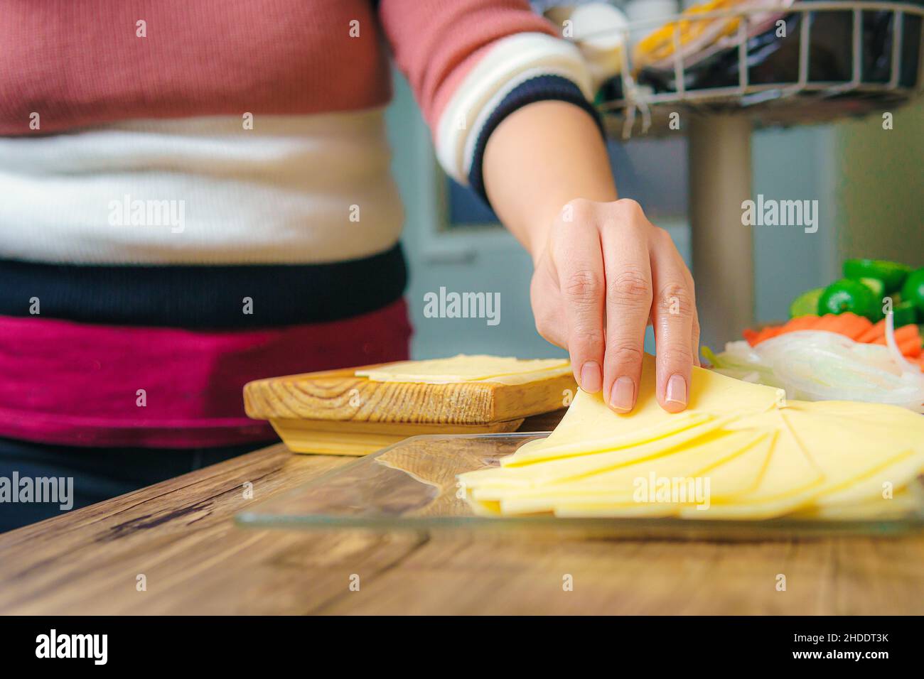 On the table there are slices of yellow cheese, a woman's hand can be seen taking a slice to arrange it or to eat. Stock Photo