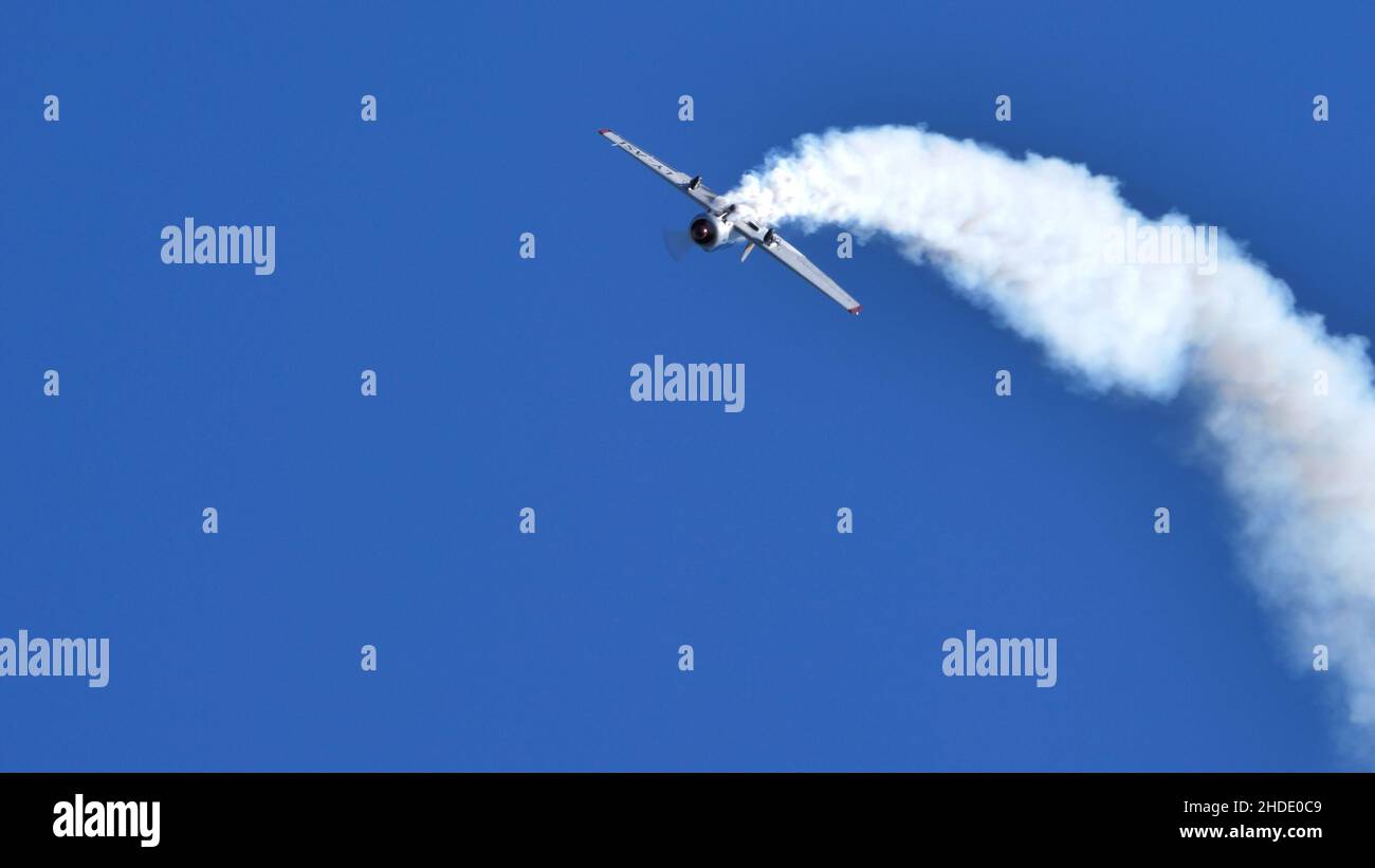 Thiene Italy OCTOBER, 16, 2021 Acrobatic plane upside down with white smoke in blue sky with huge copy space. Yakovlev Yak-52 by YAK Italia Stock Photo