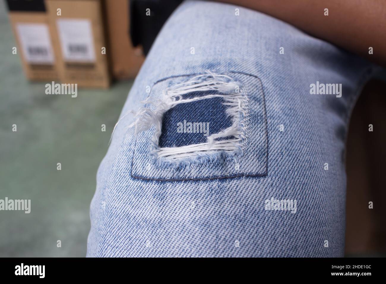 Close up on jeans with hole on the knee. A fix of ripped jeans using a patch of similar color cloth behind. Stock Photo