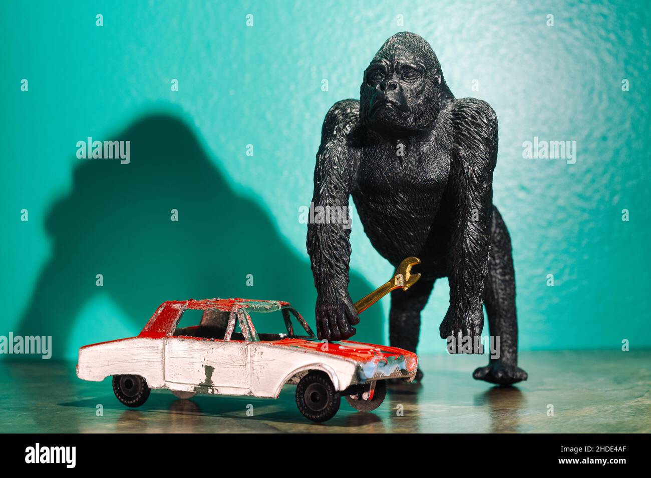 Toy gorilla holding wrench to work on old red car concept Stock Photo