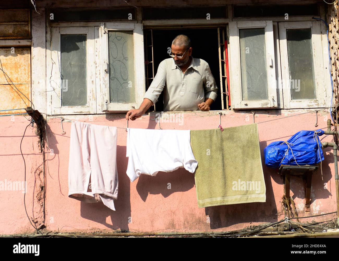 A man hanging washed laundry on a rope outside his home window in Mumbai, India. Stock Photo