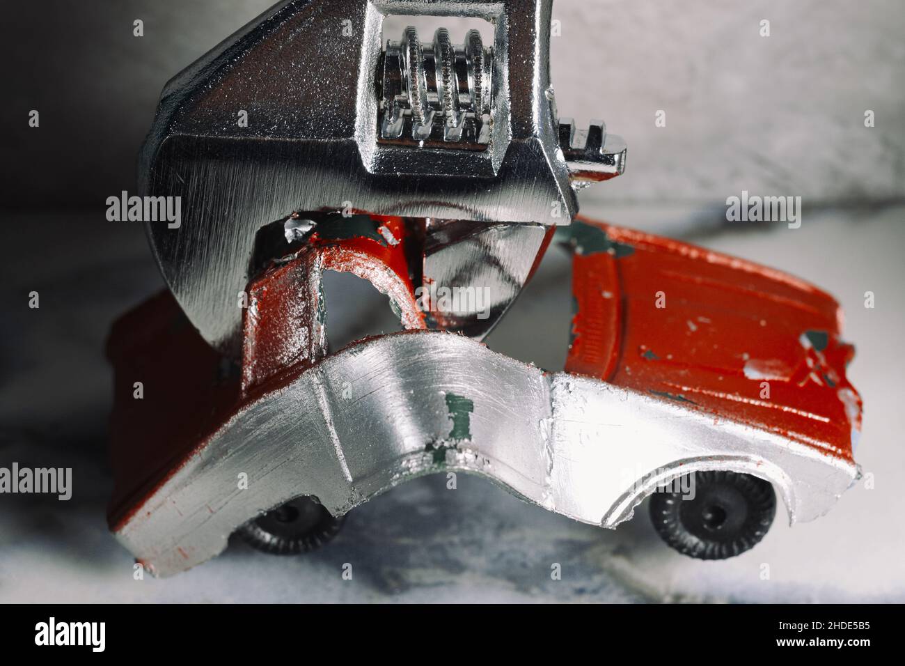 Macro concept giant wrench destroys toy car at crooked car mechanic shop Stock Photo