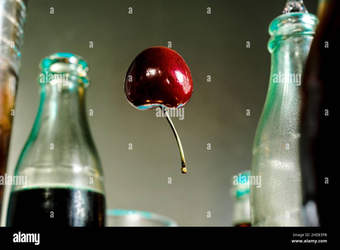 Cherry floats through the air like a balloon surrounded by cola bottles Stock Photo