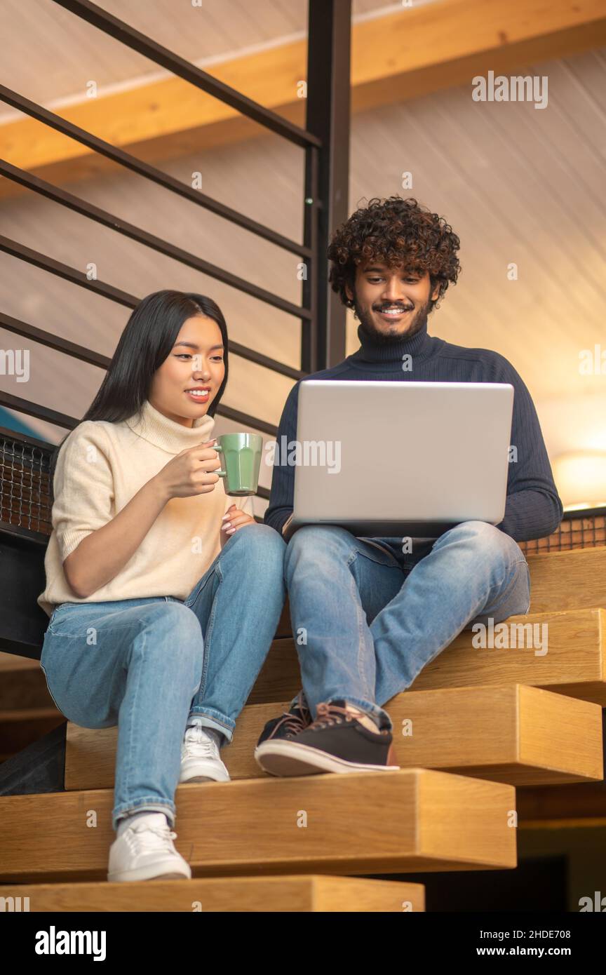 Man and woman looking at laptop sitting on stairs Stock Photo