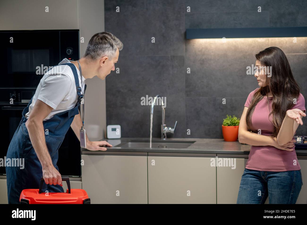 Questionning Plumber Woman with question gesture and plumber looking at broken faucet Stock ...