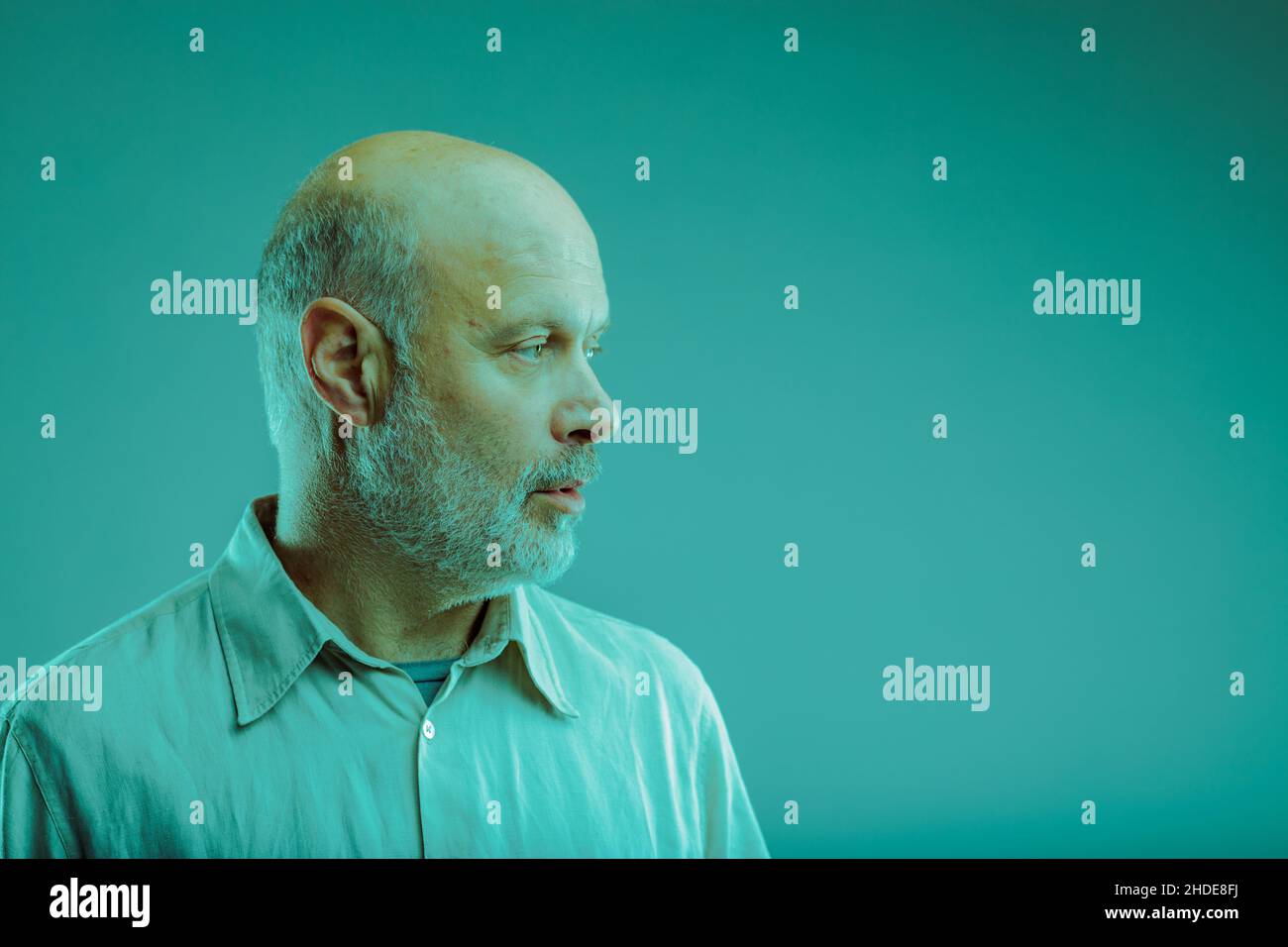 Thoughtful balding senior man with beard looking aside towards blank copyspace on a blue color toning Stock Photo
