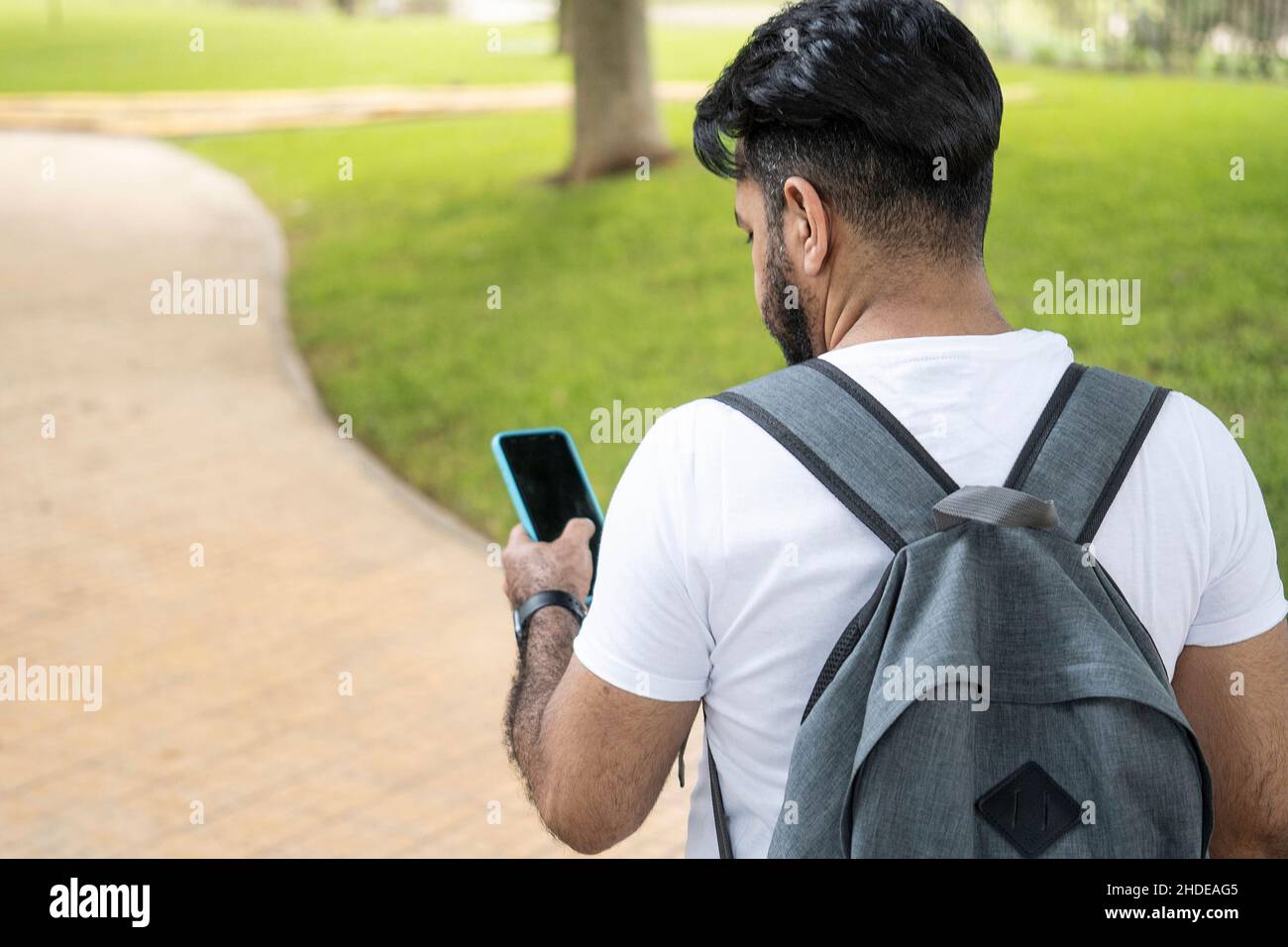photo of back of latin man with a backpack looking at his cell phone looking for the road Stock Photo