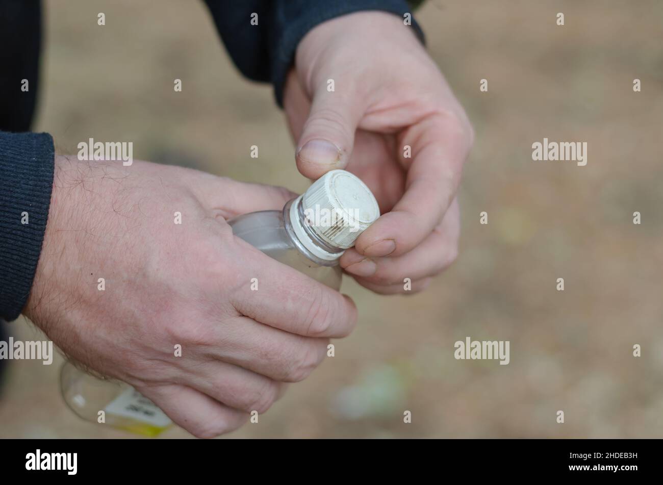 Two hands of a grown man holding a plastic bottle. Liquid fire starter